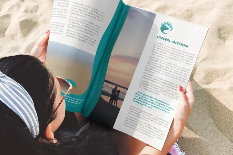 Frau liest Umweltmagazin am Ostseestrand – Arkona Strandresidenzen sind Teil der Rügener Initiative „Ohne Meer wird schwer“