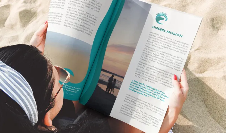 Frau liest Umweltmagazin am Ostseestrand – Arkona Strandresidenzen sind Teil der Rügener Initiative „Ohne Meer wird schwer“