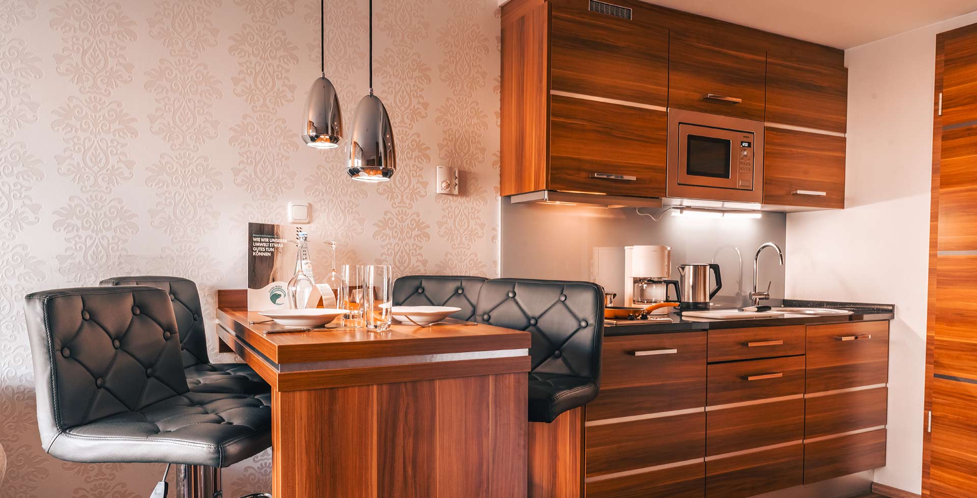 Eine hölzerne Küche und links daneben eine Theke mit grauen gepolsterten Barhockern im Apartment Hotel auf Rügen.