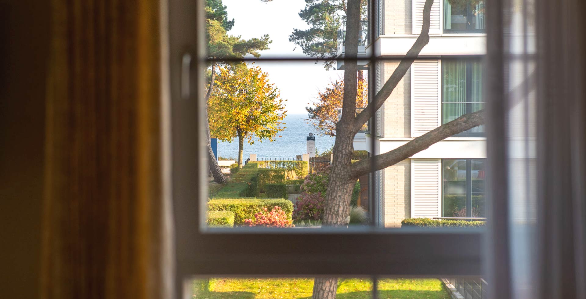 Blick aus dem Fenster des Apartment Hotels auf Rügen auf die Ostsee mit Garten und herbstlichen Bäumen.