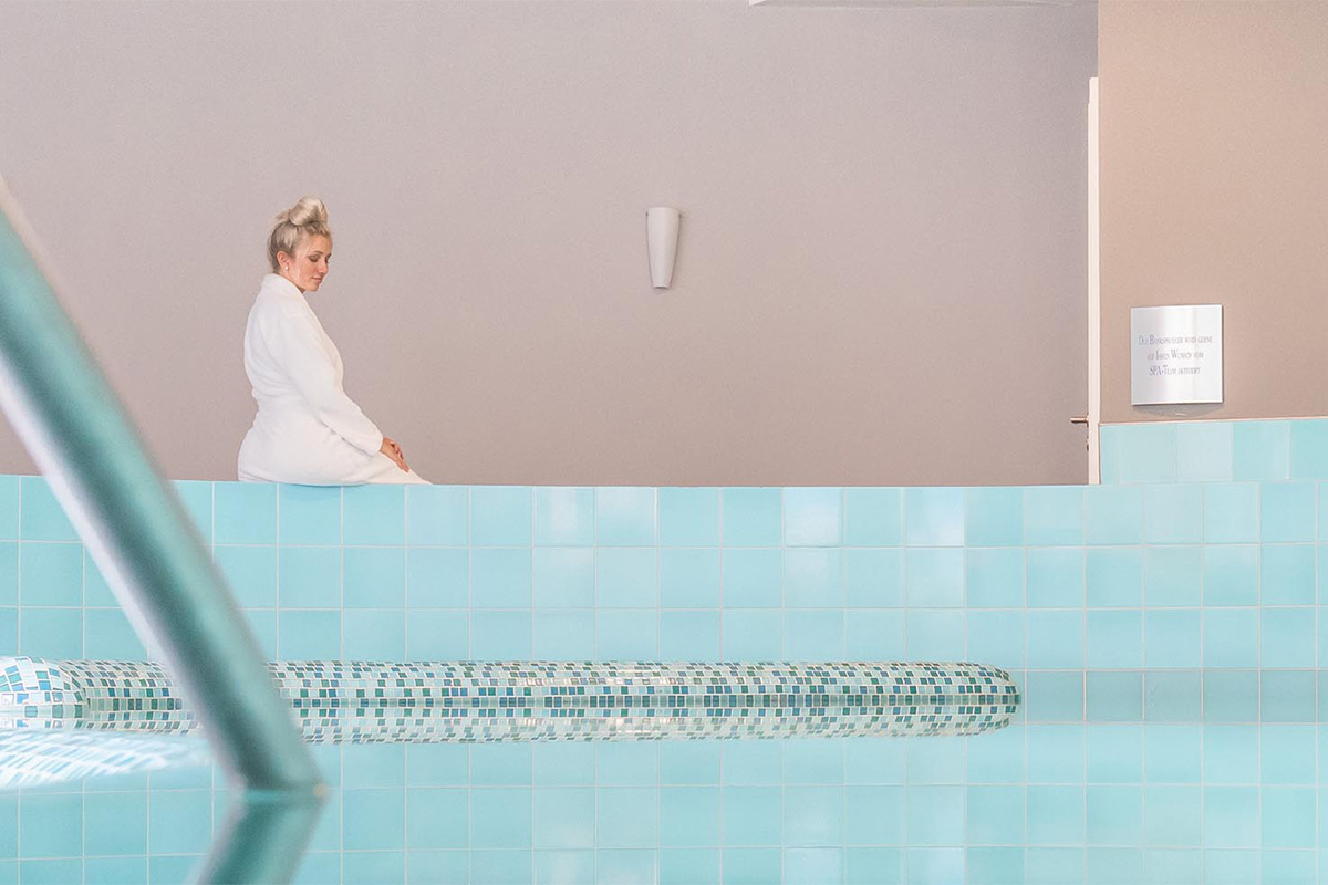 Eine blonde Frau sitzt am Beckenrand des Hotelpools bereit für die Wassergymnastik im Ostseeurlaub bei Private Palace Hotels & Resorts.