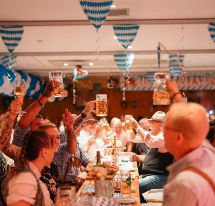 Gäste feiern mit erhobenen Armen beim Binzer Oktoberfest mit traditioneller Kulinarik und festlicher Dekoration bei Private Palace Hotels & Resorts.