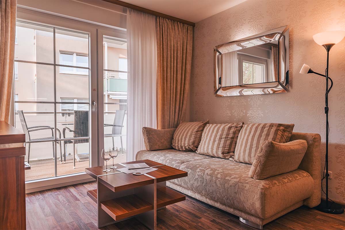 Wohnbereich im Apartment der Arkona Strandresidenzen Binz mit gemütlichem Sofa, Couchtisch und Balkonblick