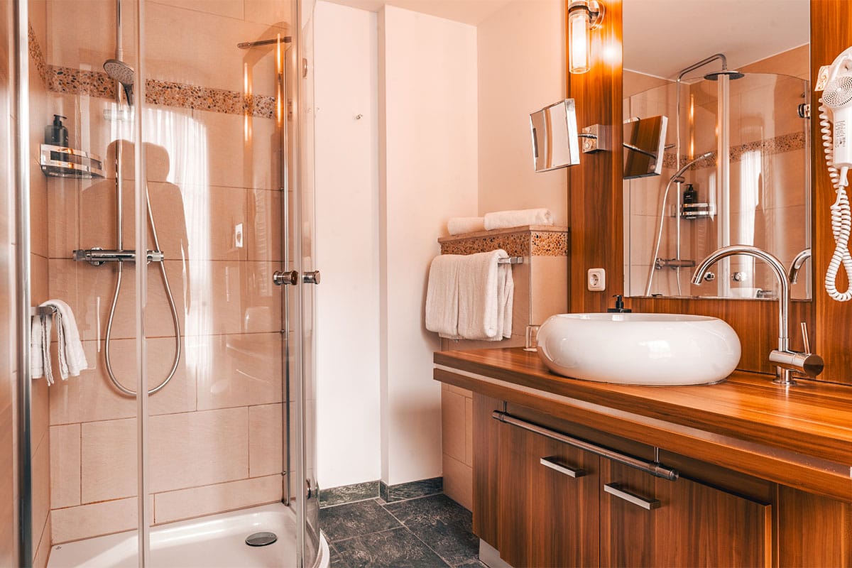 Badezimmer im Apartment der Arkona Strandresidenzen Binz mit Glasdusche, Waschbecken und Holzverkleidung