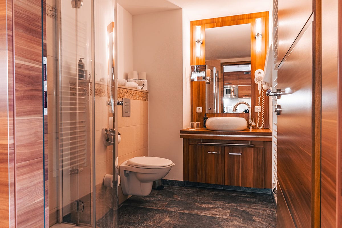 adezimmer im Deluxe Apartment der Arkona Strandresidenzen Binz mit Dusche, Waschtisch, Spiegel und Holzelementen