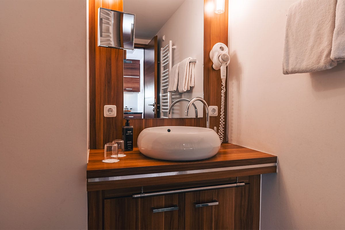 Waschbecken im Deluxe Apartment der Arkona Strandresidenzen Binz mit runder Schale, Wandspiegel und Föhn