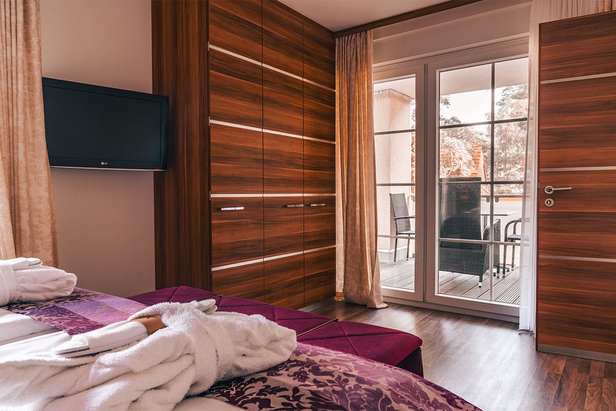 Blick vom Bett auf Schrankwand, Fernseher und Balkontür im Suite Apartment der Arkona Strandresidenzen Binz