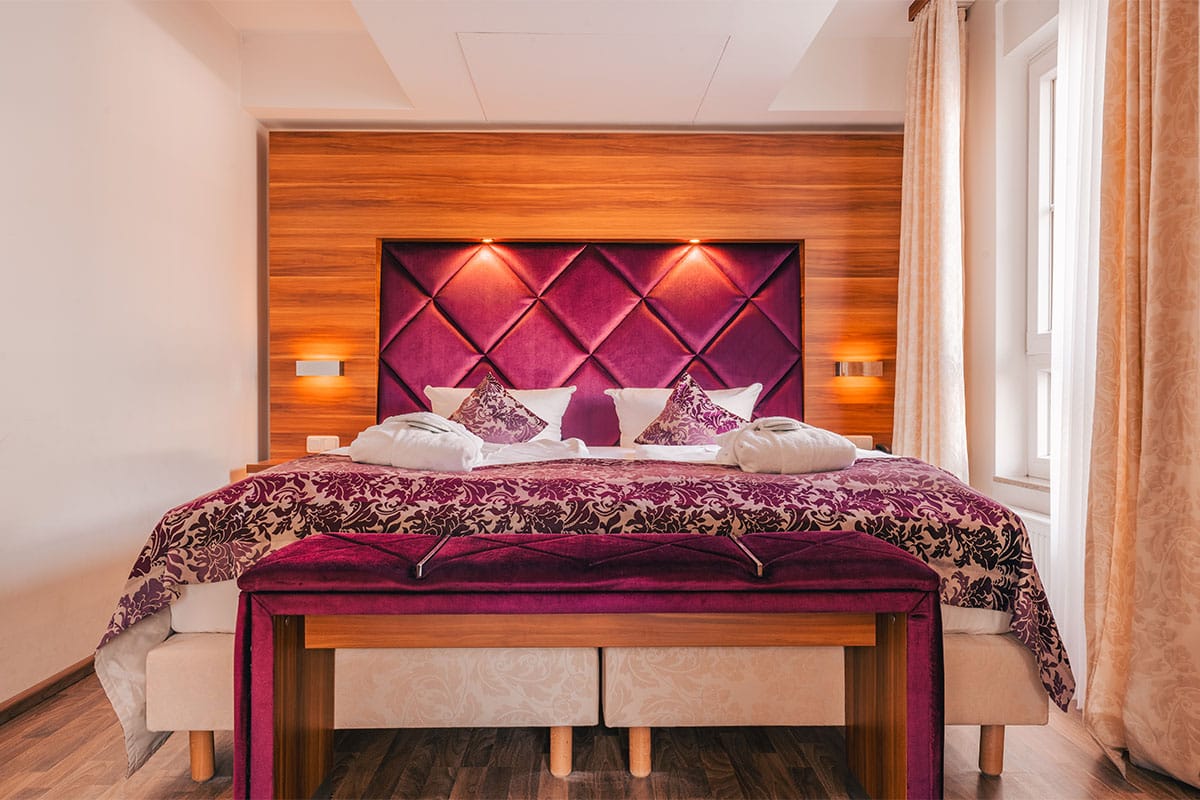 Doppelbett im Suite Apartment der Arkona Strandresidenzen Binz mit dekorativen Kissen und Tagesdecke in Lila